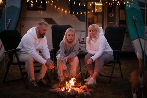 A family cooks sausages on a bonfire near their motorhome in the woods photo