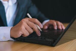 Close-up of businessman working with notebook computer and using pen to take notes in office desk photo