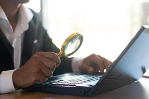 A businessman or accountant works on a computer and uses a magnifying glass to look at business documents on the office table. photo