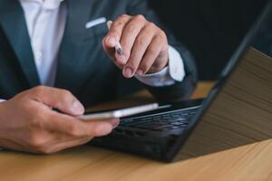 Close-up of a businessman working with a notebook computer and using a pen to take notes on work in an office desk. Thinking about work and goals. photo