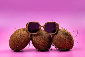 three whole coconuts and wooden glasses on a pink background photo