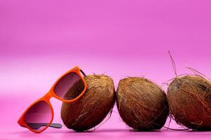 three whole coconuts and orange glasses on a pink background photo