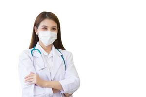 Young professional Asian woman doctor wears medical coat stands confidently and smiles she is arm crossing while she wears white lab coat and face mask in hospital while isolated white background. photo