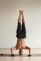 a man with a naked torso does yoga standing on his head indoors. Fitness Trainer photo