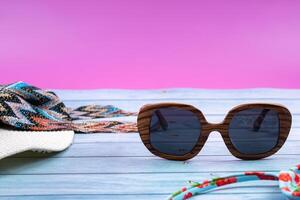 Top view of a straw white hat with glasses and a swimsuit, lying on a blue wooden background.Summer vacation concept photo