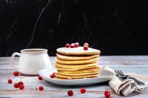 morning breakfast of pancakes with cranberries and powdered sugar and a cup of coffee on a wooden table photo