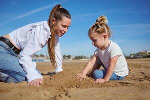 Close up portrait of happy of mother and daughter building castle in sand at beach photo