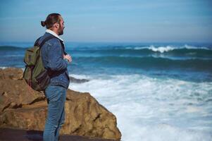 Absorbed bearded man traveling alone, standing on a cliff and looking at horizon, enjoying the view of beautiful nature photo