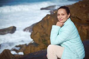 Happy woman smiling at camera, sitting on the cliff and enjoying beautiful view of Atlantic ocean. People. Tour tourism. photo