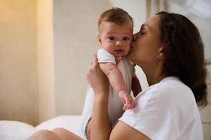 Cute baby boy looking at camera while his mother cuddling and kissing him photo