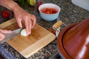 recortado ver de el manos de un cocinero corte cebolla en dos mitades en un de madera junta, utilizando un cocina cuchillo. foto