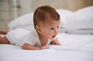 Adorable baby boy 4 months old in white sunny bedroom. Newborn child relaxing in bed during tummy time. Copy ad space photo