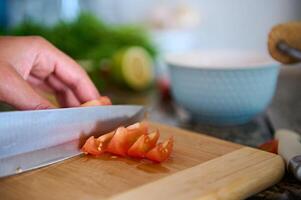 Cropped view of a chef cook slicing red juicy tomatoes on a wooden board photo