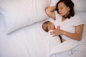 The concept of co-sleeping and breastfeeding. View from above of a sleeping mother breastfeeding her newborn baby photo