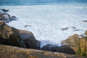 Nature background waves crashing coast, making white foam while breaking on rocky beach. Slow motion photo