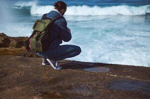 Traveler adventurer sitting on the edge of a rocky cliff, overlooking view of Atlantic ocean with breaking waves photo