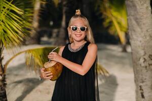 Portrait of a cheerful 9-year-old girl with a coconut cocktail on the background of palm trees on an exotic beach.little Girl with a coconut on the beach of the island of Mauritius photo