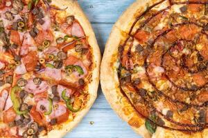 Two different delicious big pizzas on a blue wooden background photo