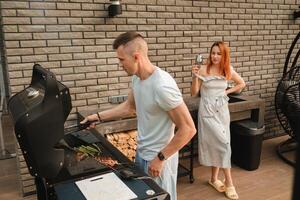 un casado Pareja cocineros A la parrilla carne juntos en su terraza foto