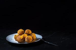 cheese balls with garlic and dill inside for a snack in a white plate on a black background photo