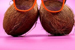 Two whole coconuts and orange glasses on a pink background. photo