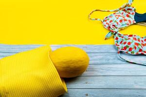 Top view of a swimsuit and a melon in a bag, lying on a blue wooden and yellow background.Summer vacation concept photo