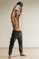 A man with a naked torso is engaged in strength fitness using a rubber loop indoors photo