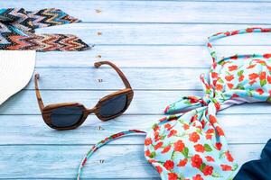 Top view of a straw white hat with glasses and a swimsuit, lying on a blue wooden background.Summer vacation concept photo