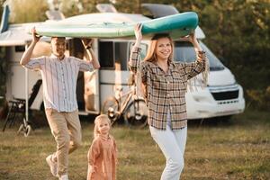 a young family is playing next to their mobile home. Dad and mom are carrying a sup board and daughter is walking next to photo