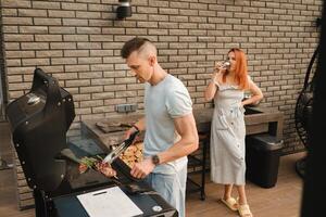 A married couple cooks grilled meat together on their terrace photo