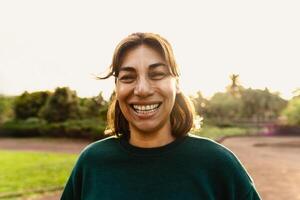 contento latín mujer teniendo divertido sonriente en el cámara en un público parque foto