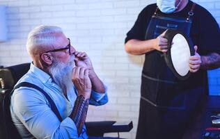 Male hairdresser cutting hair to hipster senior client while wearing face surgical mask - Young hairstylist working in barbershop during corona virus outbreak - Health care and haircut salon concept photo