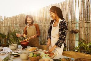 Happy Southeast Asian sisters having fun preparing Thai food recipe together at house patio photo