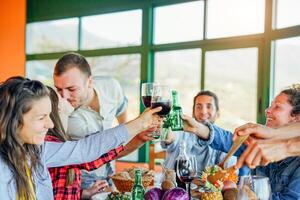 Happy friends cheering with glasses of red wine and beers at lunch - Young people having fun toasting and drinking together in a vineyard house - Friendship and youth lifestyle concept photo