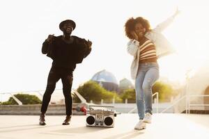 joven afro amigos bailando al aire libre mientras escuchando a música con inalámbrico auriculares y Clásico boombox foto
