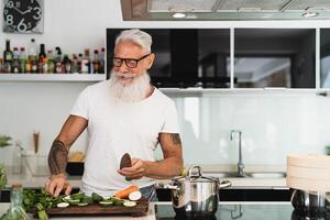 Happy senior man having fun cooking at home - Elderly person preparing health lunch in modern kitchen photo