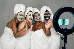 Happy multiracial females having skin care spa day while streaming on social network with mobile smartphone - People selfcare concept photo