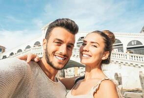 hermosa joven Pareja tomando un selfie disfrutando el hora en su viaje a Venecia - novio y Novia tomando un imagen mientras en pie debajo el puente de rialto en Venecia en su Luna de miel foto