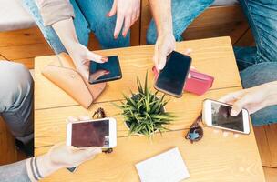 Millennial friends using their mobile smart phones in bar - Young people connecting on new trends social networks - Influencer, media and technology concept photo