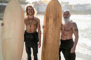 Happy fit surfers with different age surfing together at sunset time - Extreme sport lifestyle and friendship concept photo