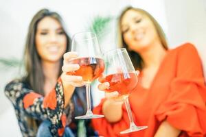 Young women toasting glasses of rose wine in their home - Happy sisters enjoying their time together drinking cocktails and having fun - Concept of people, drinks, lifestyle - Focus on glass photo