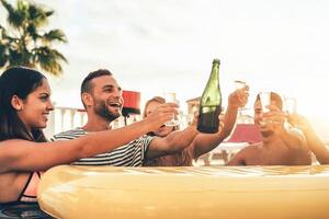 Happy friends toasting champagne at pool party  - Young people having fun drinking sparkling wine in luxury tropical beach resort at sunset - Holidays, vacation, summer and youth lifestyle concept photo