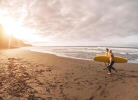 contento amigos teniendo divertido surf en puesta de sol hora - surfistas padre y hijo corriendo en playa - deportivo salud personas estilo de vida y extremo deporte concepto foto