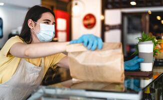 bar propietario trabajando solamente con tomar lejos pedidos durante corona virus brote - joven mujer trabajador vistiendo cara quirúrgico máscara dando eliminar comida a clientes - cuidado de la salud y comida bebida concepto foto