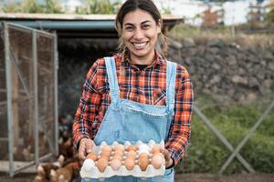 Mature female farmer picking up fresh eggs in henhouse garden - Farm people lifestyle concept photo