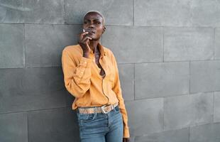 Afro senior woman smoking cigarette while standing against urban wall photo