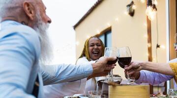 Happy multiracial seniors toasting with red wine glasses together on house patio dinner - Elderly lifestyle people concept photo