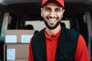 joven mensajero entrega hombre sonriente dentro el cámara mientras en pie en frente de su camioneta transporte foto