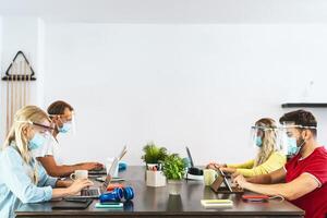 Young people working in co-working creative space wearing surgical mask protection for preventing corona virus spread - Social distancing, content creator startups and technology concept photo