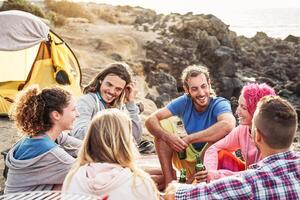 grupo de contento amigos cámping siguiente el playa a puesta de sol - joven personas teniendo divertido y Bebiendo cerveza al aire libre - milenario, verano, vacaciones y juventud Días festivos estilo de vida concepto foto